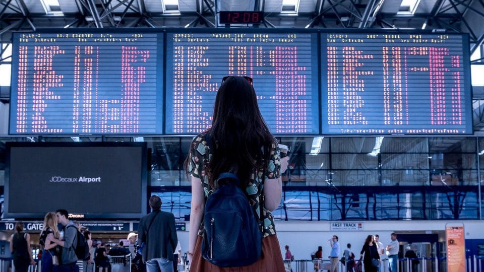 femme devant un panneau de destination dans un aéroport